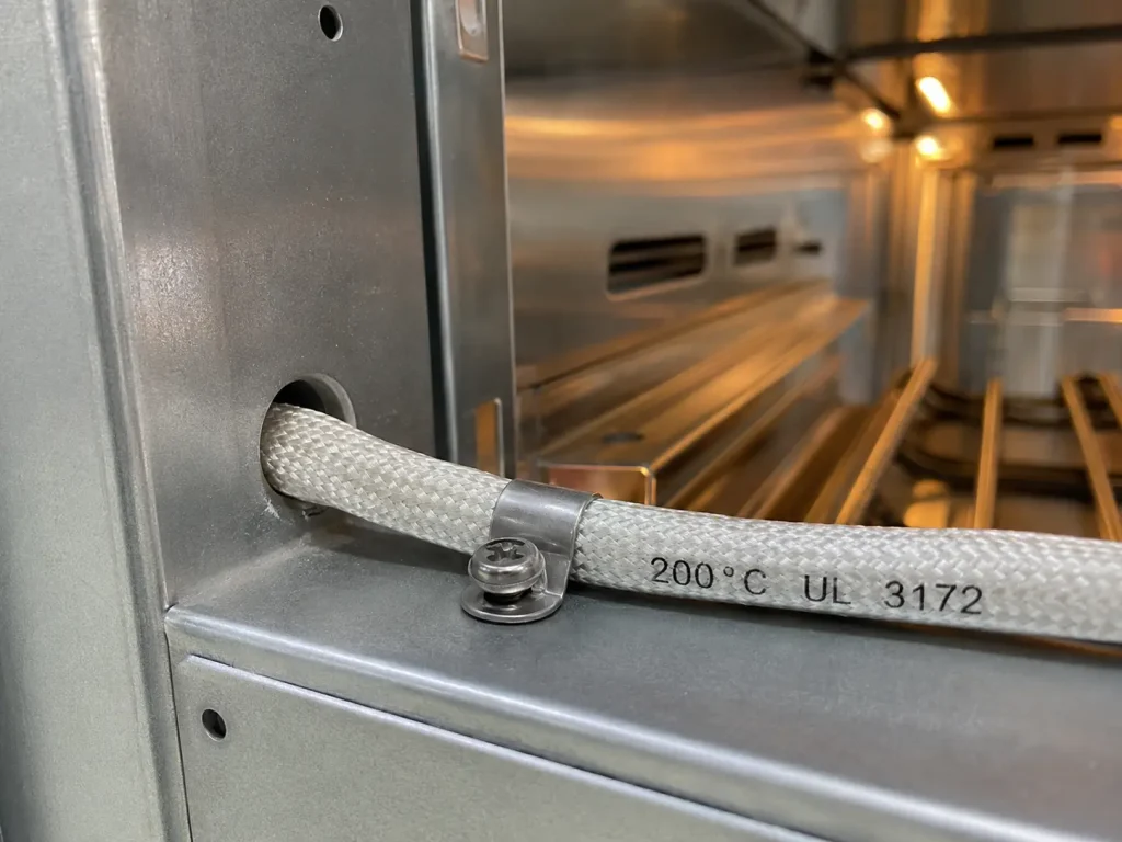 UL 3172 braided silicone wire routed at metal-edge contact point inside exported industrial oven equipment